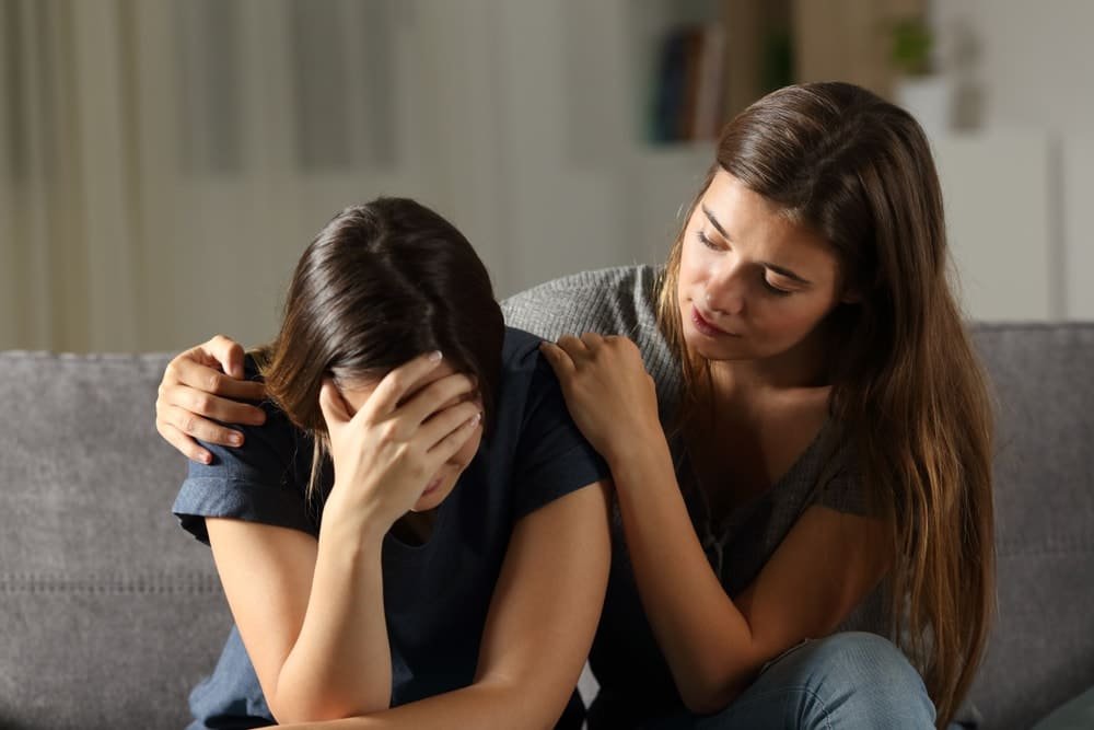 mujer tratando de consolar a otra mujer triste en un sofá